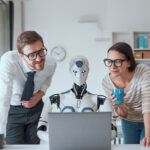Due professionisti osservano un robot umanoide al computer in ufficio, rappresentando l’uso dell’intelligenza artificiale come supporto nel project management.