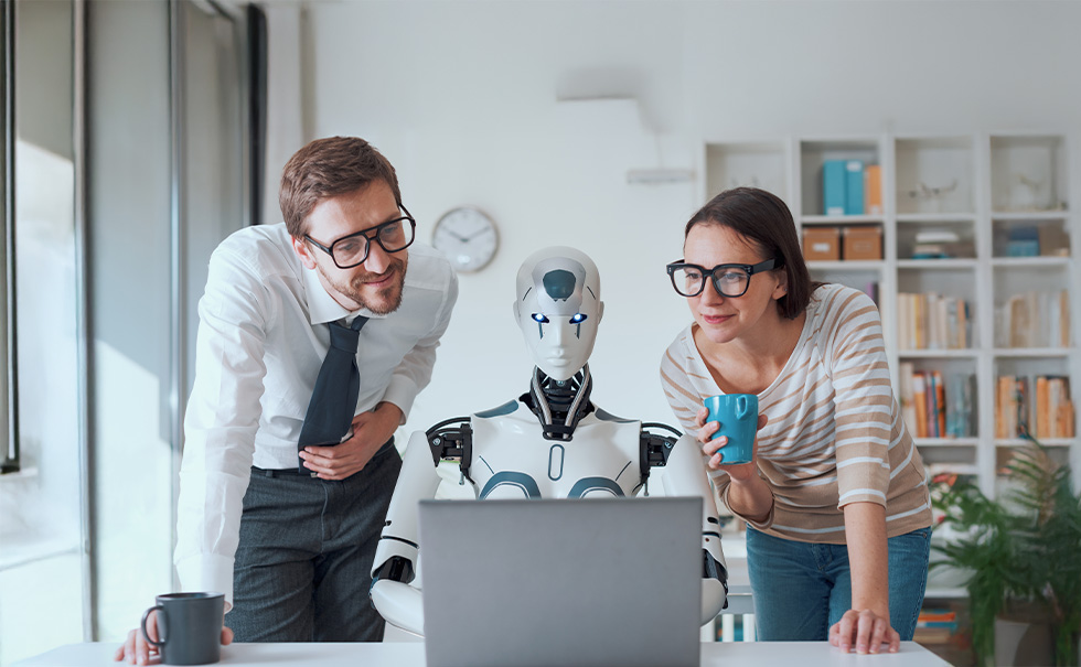 Due professionisti osservano un robot umanoide al computer in ufficio, rappresentando l’uso dell’intelligenza artificiale come supporto nel project management.