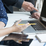 immagine generica, tavolo da lavoro con laptop e due persone visibili parzialmente